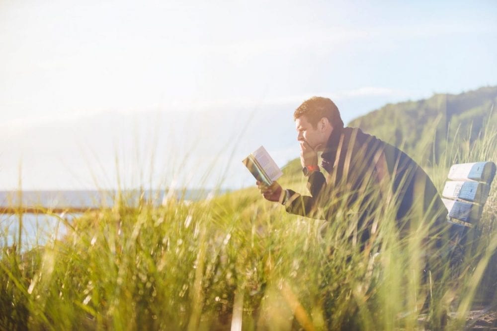 En mann som sitter på en benk og lesere en bok med engasjerende innhold